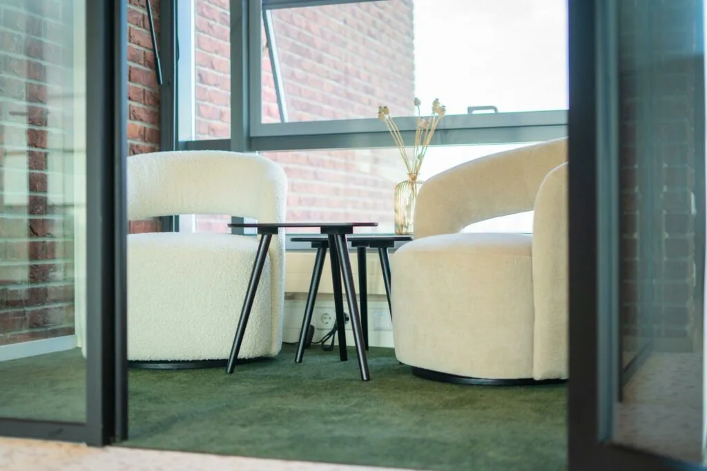 Twee moderne fauteuils met ronde vormen en een set zwarte bijzettafels in een zithoek aan de Joop Geesinkweg.
